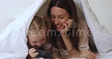 快乐的30岁妈妈和快乐的小女儿躺在羽绒被下面。